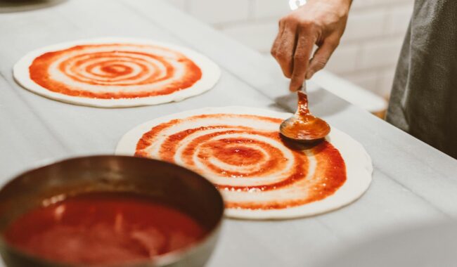 person putting pizza sauce on the dough