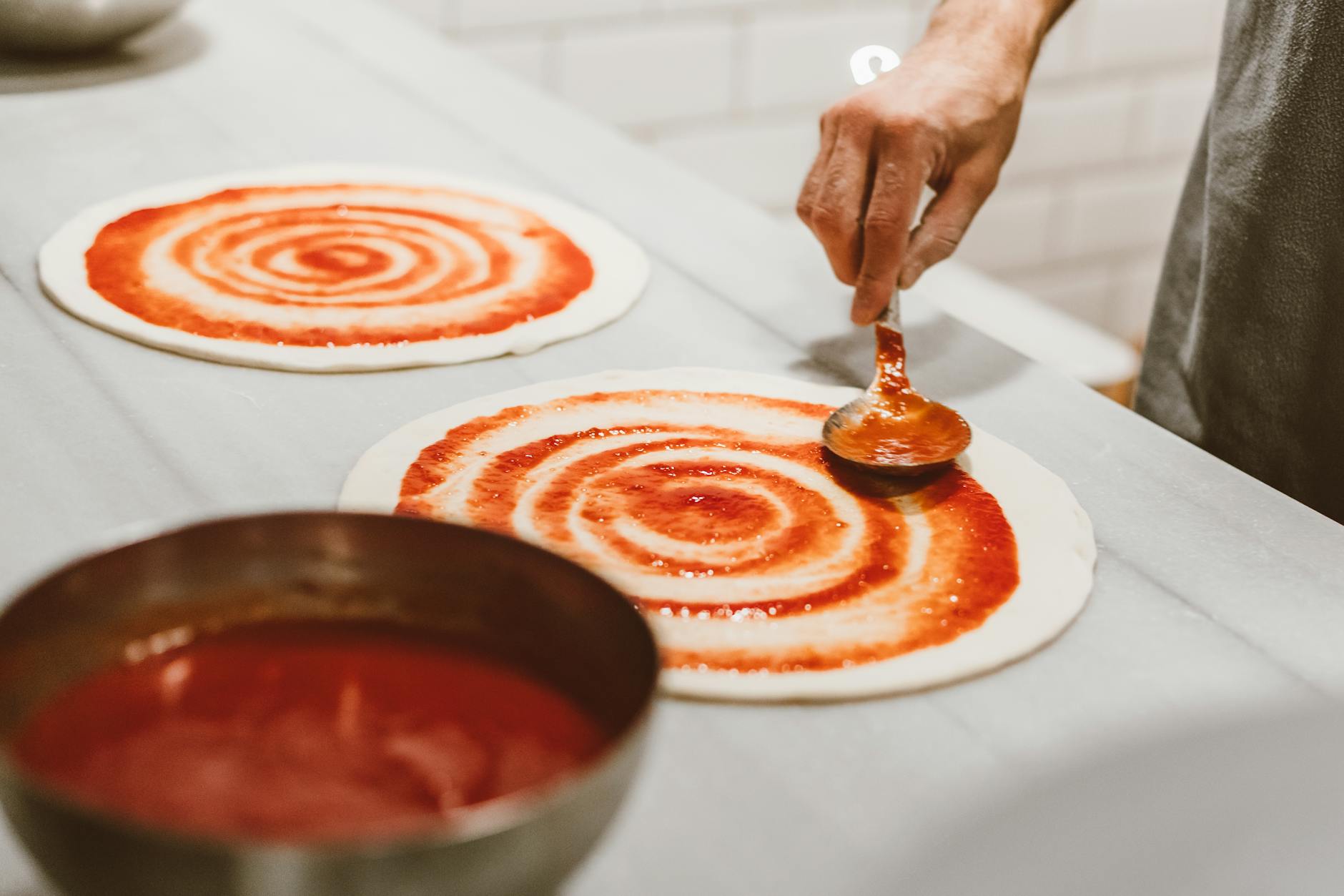 person putting pizza sauce on the dough